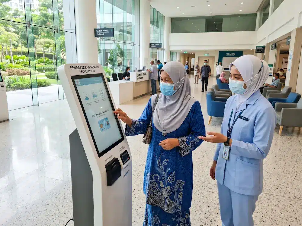 Patient using an Arvia interactive kiosk for self check-in at a modern Malaysian hospital lobby